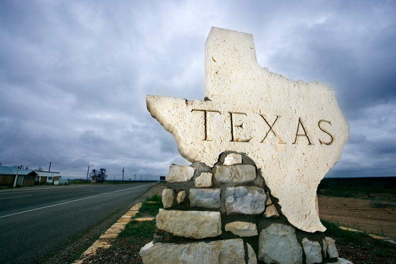 A stone Texas marker beside the highway under a stormy sky